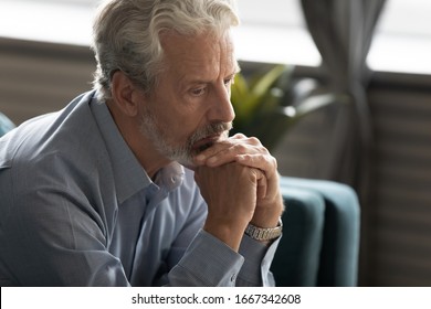 Unhappy Middle-aged 60s Man Sit On Couch Look In Distance Thinking Mourning At Home, Sad Depressed Mature Old Male Feel Lonely Abandoned Pondering Remembering Past, Elderly Solitude Concept