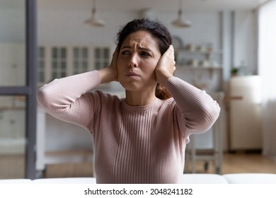 Unhappy millennial Caucasian female renter or tenant cover ears with hands hate noise at home or apartment. Upset angry woman feel depressed frustrated suffer from disturbing noisy sound in house.