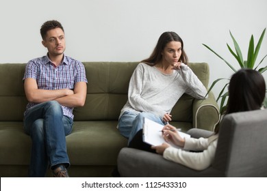 Unhappy Millennial Couple Sitting Apart On Couch Visiting Female Psychologist Listening To Counselor Helping Solving Problems In Bad Relationships, Family Therapy Session, Marriage Counseling Concept