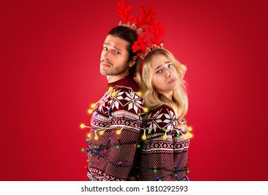 Unhappy Millennial Couple Tied With Christmas Lights On Red Background