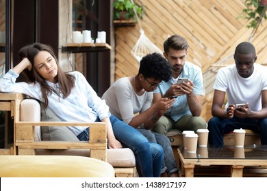 Unhappy millennial girl sit alone aside feel bored at group meeting with friends in café, diverse young people busy using smartphones addicted to gadgets, annoyed female lack communication - Powered by Shutterstock