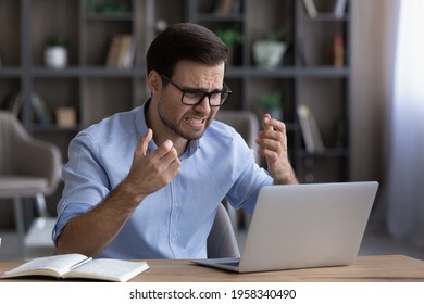 Unhappy millennial male employee work online on laptop at home office frustrated by gadget error or mistake. Angry young Caucasian man stressed with computer operational problem or breakdown.