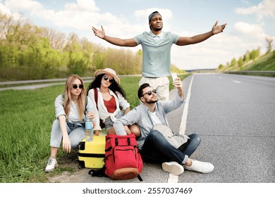 Unhappy millennial tourists sitting on roadside, cannot catch car, waiting for too long, having no smartphone connection. Young friends hitchhiking on highway, having problem finding free ride - Powered by Shutterstock