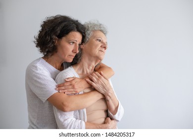 Unhappy mother and daughter hugging. Upset middle aged woman hugging pensive senior mother and looking aside isolated on grey background. Emotion concept