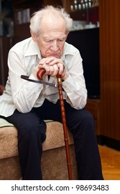 Unhappy Old Man Sitting On A Bed And Holding His Cane