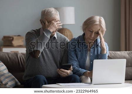 Unhappy old wife and husband sit on couch in living room with laptop and calculator manage family finances, feel desperate due debts, unpaid bills, lack of money to pay monthly bills or bank mortgage