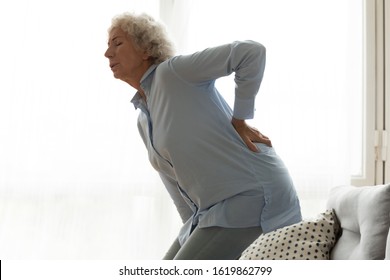 Unhappy Older Woman Feeling Sudden Strong Pain, Touching Lower Back, Standing In Living Room At Home, Upset Mature Female Feeling Unwell, Health Problem, Suffering From Backache, Strain, Rheumatism