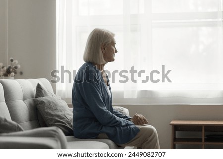 Unhappy older woman sit on sofa in living room, feels lonely, think over health problems, suffers from loneliness. Faced up with loss or illness disorder, having depression or apathy, melancholic mood
