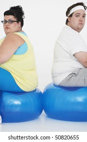 Unhappy Overweight Man And Woman Sitting Back To Back On Exercise Balls, Portrait