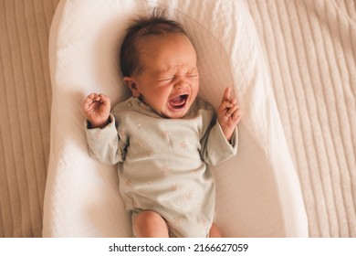 Unhappy Sad Baby Lying In Bed Crib Wake Up And Crying At Home In Room. Sad Sick Newborn Child Shouting With Stomach Pain And Colics Close Up. Healthcare. Childhood. 