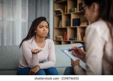 Unhappy Sad Black Millennial Woman Patient Talking With European Doctor In Clinic Interior. Medicine, Professional Help, Depression Treatment And Support, Patient Care, Therapy And Health Problems