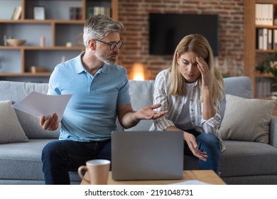 Unhappy Sad Senior Caucasian Man And Woman Work With Documents And Laptop, Pay Taxes And Quarrel In Living Room Interior. Stress, Debt, Bill Problems, Home Bookkeeping, Credit Mortgages And