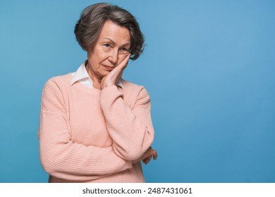 Unhappy sad senior woman suffering from terrible toothache. Frustrated female pensioner in blue shirt holding hand on her face having worried uneasy facial expression, thinking about her future. - Powered by Shutterstock