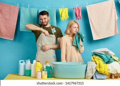 Unhappy Sad Young Man And Woman In Aprons Are Allergic To Washing Powder, Soap, Bad Detergent. Couple Expressing Negative Emotion While Doing Laundry.what Awful Smell