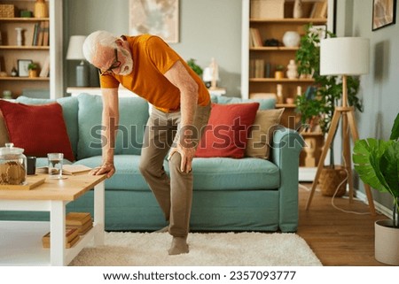Unhappy senior man suffering from knee ache at home
