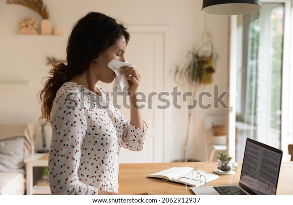 Unhappy sick\
woman, adult student, remote employee staying at home due to flu\
infection, suffering from snuffles, seasonal allergy, blowing runny\
nose, covering face with paper\
tissue
