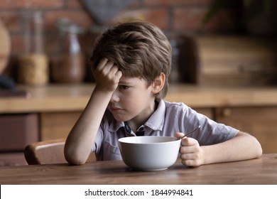 Unhappy Small Caucasian Boy Child Sit At Kitchen Table Have No Appetite For Healthy Breakfast. Sad Upset Little 7s Kid Refuse To Eat Nutritious Meal Or Food At Home. Children Healthcare Concept.