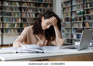 Unhappy Stressed Young Hispanic Female Student Feeling Tired Preparing For Examination, Reading Books, Web Surfing Information, Writing Notes In Copybook, Overworking In Modern College Library.