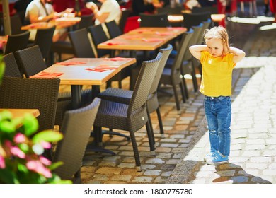 Unhappy And Stubborn Toddler Girl In Outdoor Restaurant. Misbehaving Child Outdoors. Terrible Twos And Kid Tantrums Concept