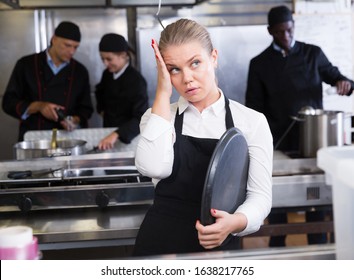 Unhappy And Tired Young Waitress Waiting Ordered Dishes In Restaurant Kitchen

