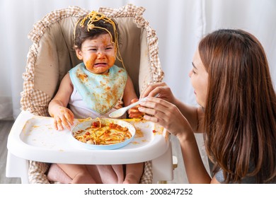 Unhappy Toddler Child With Tomato Sauce On Her Face Crying With Her Mother Sitting Together Beside In The Room. Upset Messy Little Girl Mix Race Hungry Eating Spaghetti With Mom At Home.