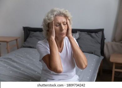 Unhappy unhealthy mature woman touching temples, suffering from strong headache or migraine, exhausted tired middle aged female feeling unwell, suffering from insomnia, sitting on bed at home - Powered by Shutterstock