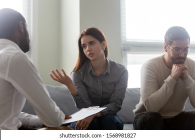 Unhappy wife talk with biracial male psychologist share relationships problems with marriage specialist at therapy session, desperate young couple consulting with counselor speak about family troubles