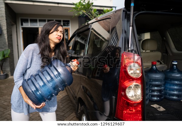 unhappy woman carrying a gallon of water at her\
house by herself
