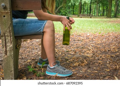 Unhappy woman drinking wine in the park and sitting on a bench - alcoholism concept