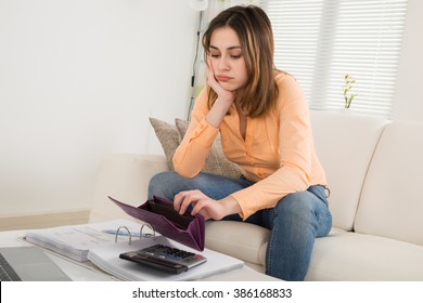 Unhappy Woman Holding Empty Purse With Calculator And Bills On Table