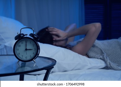 Unhappy Woman With Insomnia Lying On Bed Next To Alarm Clock At Night