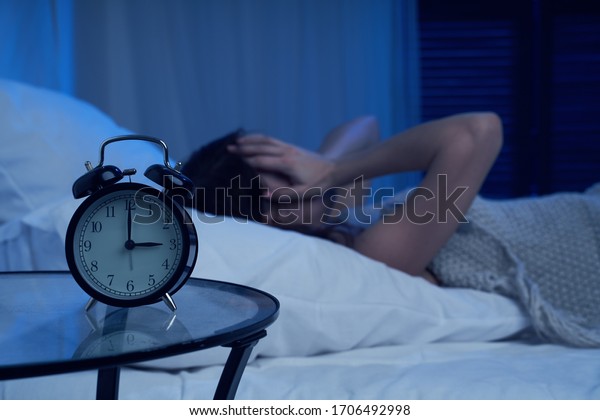 Unhappy woman with insomnia lying on bed next to\
alarm clock at night