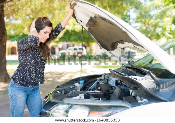 Unhappy\
woman looking at engine of broken car at\
roadside
