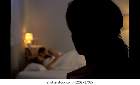 Unhappy woman looking at husband with mistress in bed, cheating, divorce reason