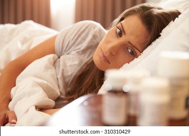 Unhappy Woman Looking At Medication On Bedside Table