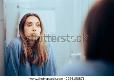 
Unhappy woman Looking in the Mirror Feeling Overwhelmed. Bored millennial girl puffing being tired and insecure
