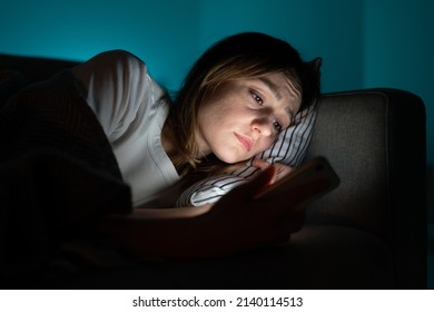 Unhappy woman lying in bed with smartphone, following ex-boyfriend on social media, sad female using mobile phone at night, can not sleep after relationship breakup, suffering from insomnia. Anxiety.