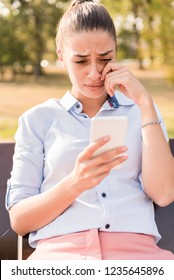 Unhappy Woman Sitting On Bench In Autumn Park With Mobile Phone Smartphone And Reading Sms