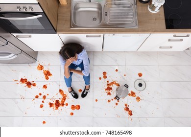 Unhappy Woman Sitting On Kitchen Floor With Spilled Food In Kitchen