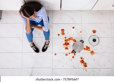 Unhappy Woman Sitting On Kitchen Floor With Spilled Food In Kitchen