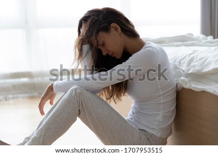 Unhappy woman touching hair, sitting on floor at home, thinking about problems, upset girl feeling lonely and sad, psychological and mental troubles, suffering from bad relationship or break up