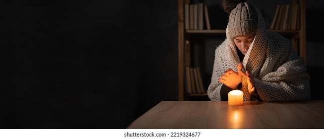 Unhappy woman warm hands on candle at cold home, shutdown of heating and electricity, power outage, blackout, load shedding or energy crisis, concept image. - Shutterstock ID 2219324677
