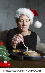 Unhappy Woman Wearing A Christmas Stocking Hat Eating A Turkey TV Dinner On A Tray Table In The Basement