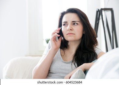 Unhappy Worried Woman Talking On Phone While Sitting On Sofa At Home