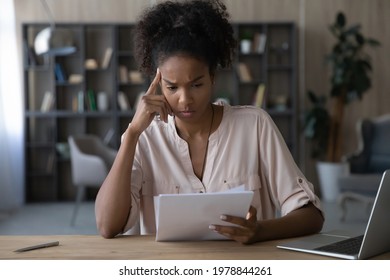 Unhappy young african american woman looking through paper document, reading unpleasant news or research report with bad results. Frustrated mixed race brazilian lady getting bank loan rejection.