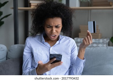 Unhappy young African American woman confused with bankruptcy or debt shopping online on cellphone with credit card. Upset biracial female buyer shop on web distressed with bank error or mistake.
