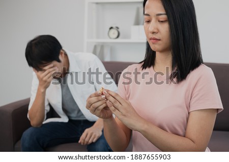Unhappy young asian couples quarrel on the couch, relationships are in trouble. The wife holding the wedding ring in disappointment and upset for her husband, which may lead to divorce.