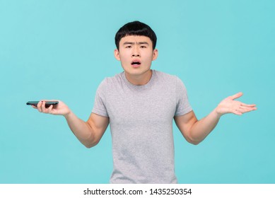 Unhappy young Asian man shrugging shoulder having trouble with his smartphone isolated on light blue studio background - Powered by Shutterstock