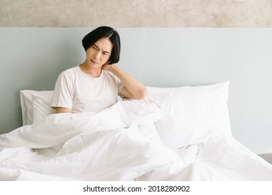 Unhappy young Asian man waking up in uncomfortable bed feeling neck ache after sleep on bad mattress in incorrect posture, sleeping on uncomfortable pillow at home. Healthcare Concept