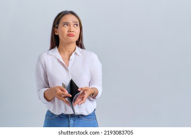 Unhappy young Asian woman holding empty wallet and looking away at copy space isolated over white background